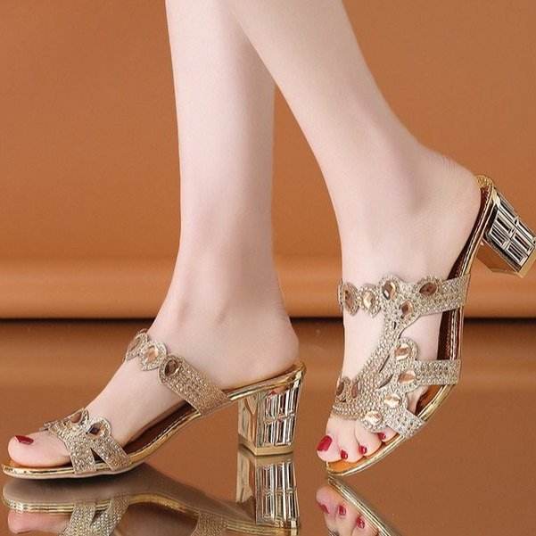 Gold high-heeled sandals with crystal embellishments on a reflective surface.